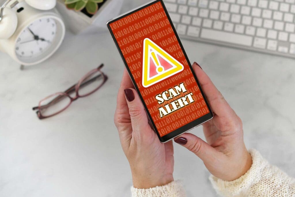 Image of a female holding a phone at desk with Scam Alert warning screen.